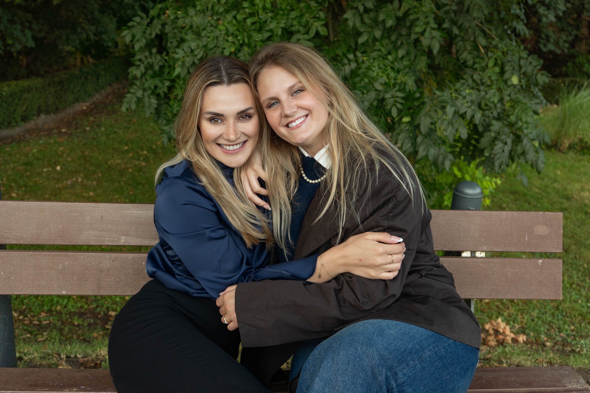Sarah und Arina umarmen sich lachend auf einer Parkbank
